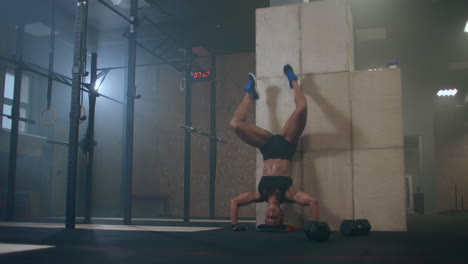 a-strong-woman-performs-vertical-push-ups-standing-on-her-head-in-the-gym.-perform-push-UPS-upside-down.-push-UPS-against-the-wall-upside-down